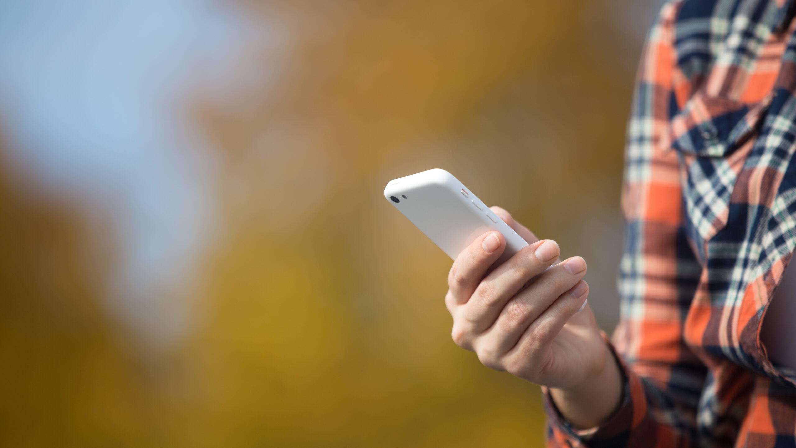 Female hand holding a mobile phone, yellow background. Fall time, close up